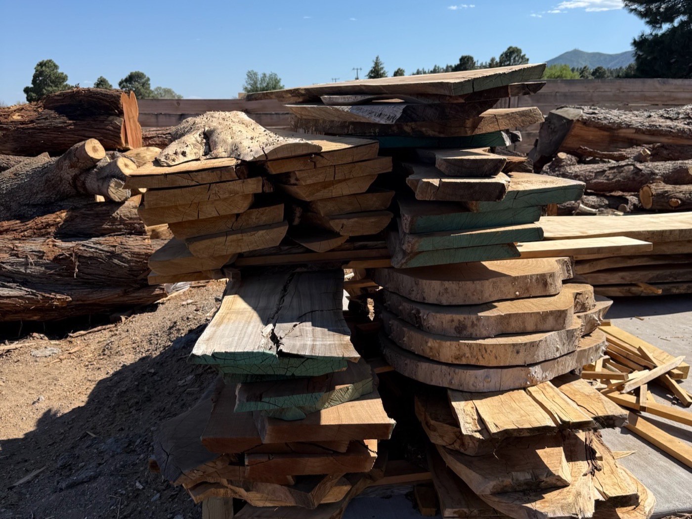 Stacked raw slabs in the yard with the Arizona mountains behind